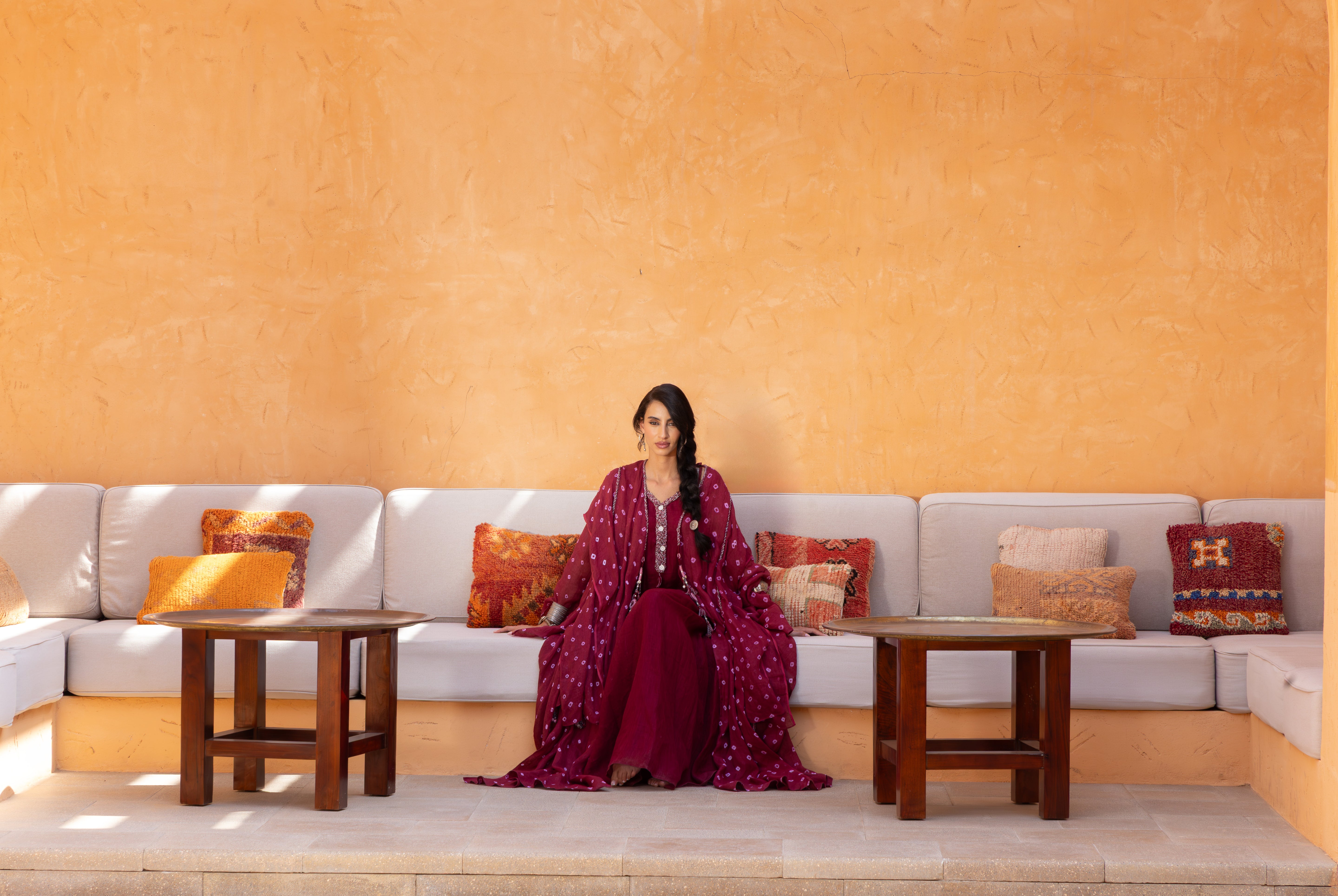 Woman in a red dress sitting on a white sofa against an orange wall.