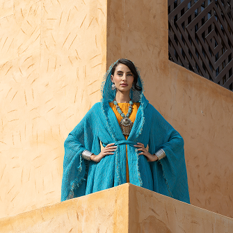 Woman in a blue dress standing on a beige wall with a textured surface