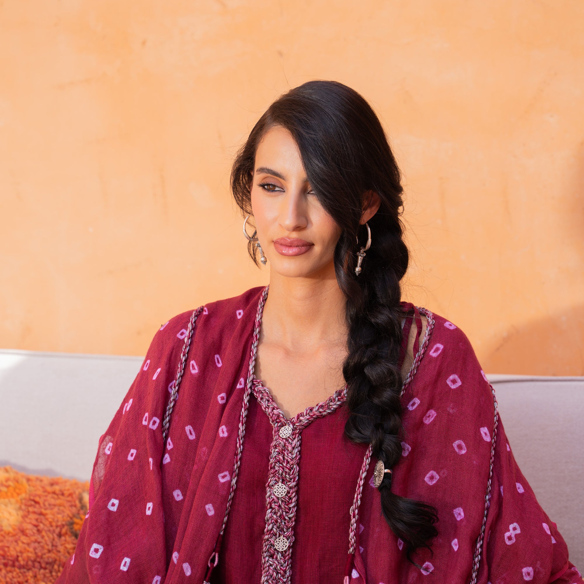Woman in a red patterned outfit sitting on a couch with an orange wall behind her