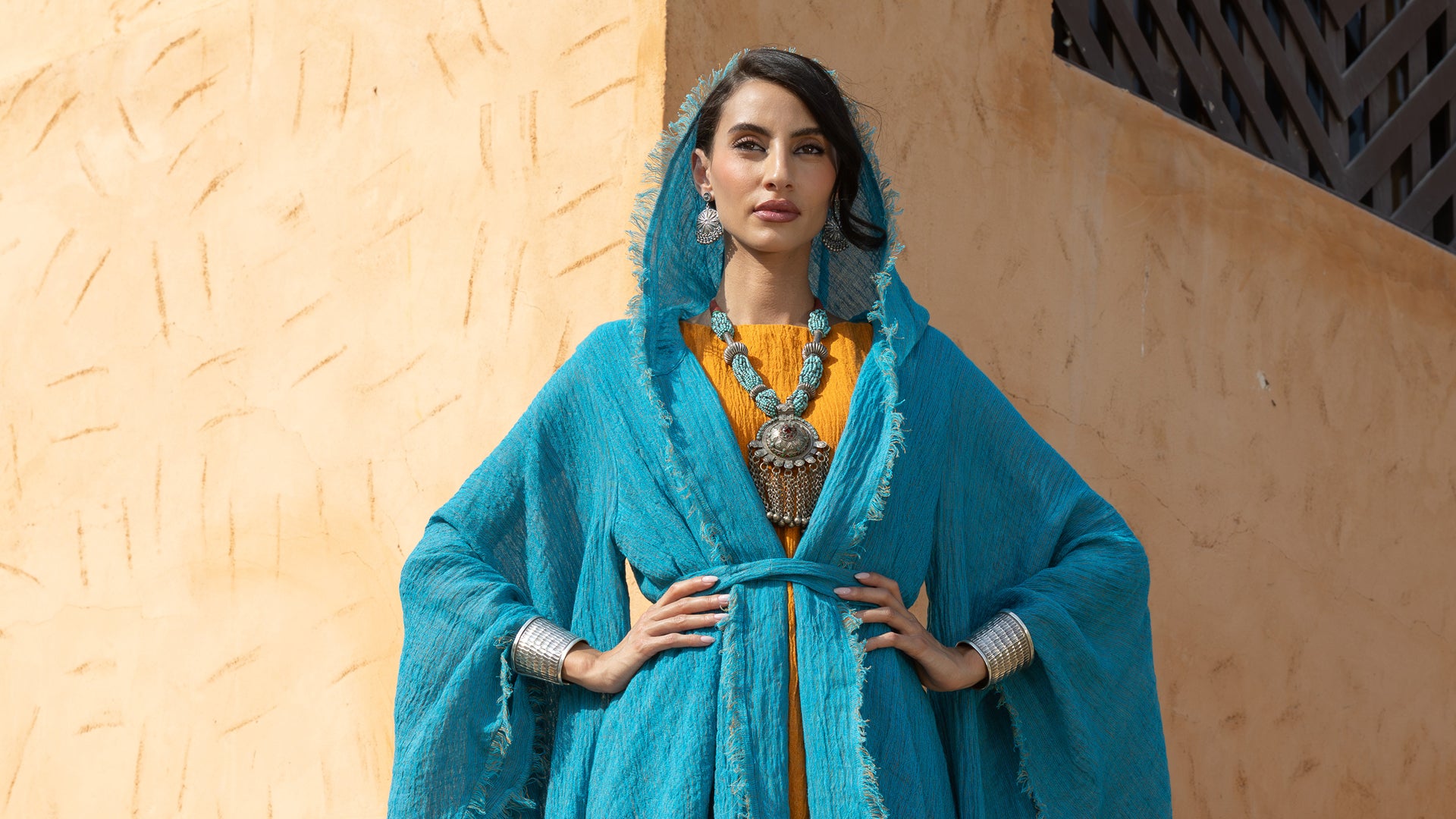 Woman wearing a turquoise traditional outfit with a beige wall background